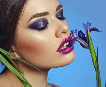 Sinnliches Frauengesicht mit lilafarbenen Lippen und lila Blüten an der Lippe
