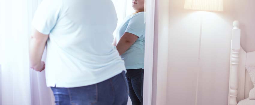 Übergewichtige Frau betrachtet sich im Spiegel